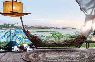 Rustikale Hängematte mit bunten Kissen und Kitesurf-Ausrüstung auf einer Holzterrasse am Meer