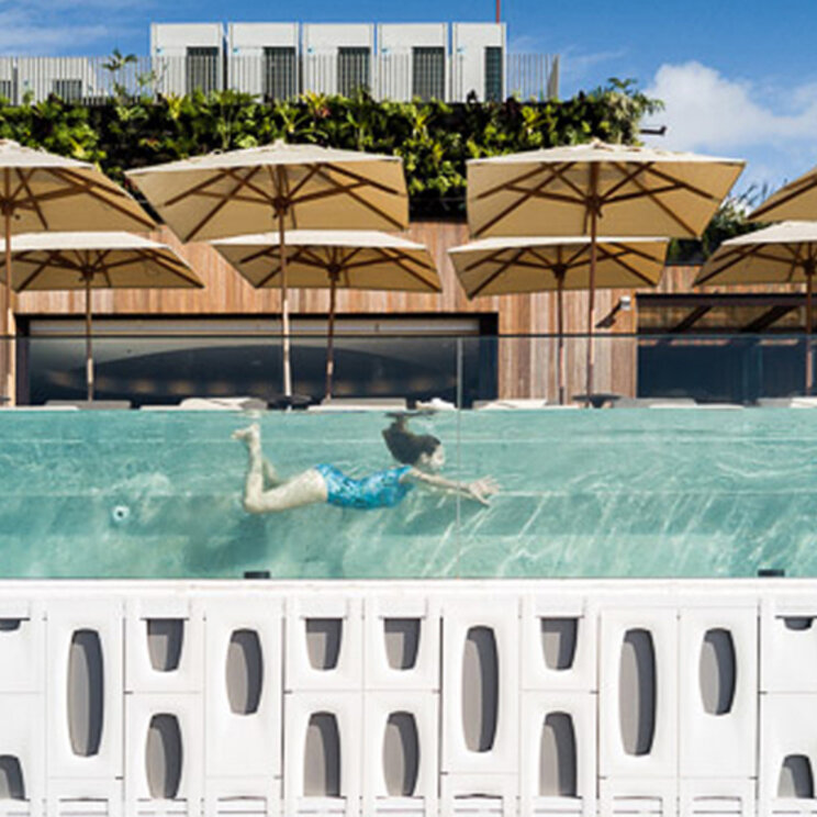 Seitenansicht des Glaspools am Emiliano Rio mit einer schwimmenden Person vor der markanten Hotel-Fassade in Rio.
