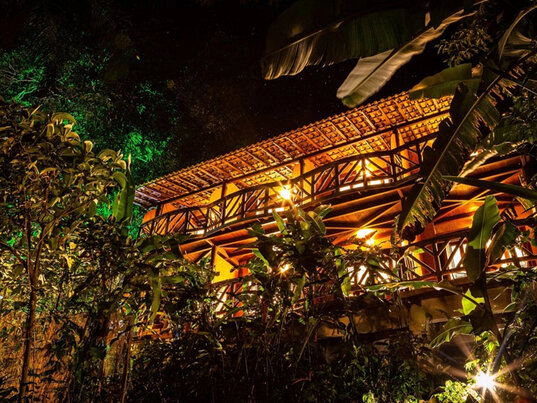 Beleuchtete Holzfassade der Pousada Naturalia bei Nacht, umgeben von tropischen Pflanzen auf Ilha Grande.