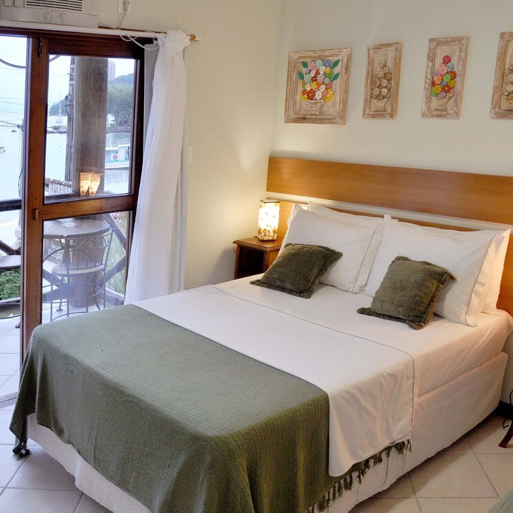 Zimmer mit Meerblick in der Pousada Caiçara auf der Ilha Grande, Brasilien, mit gemütlichem Doppelbett und Zugang zu einem Balkon.