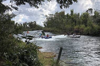 3 Schlauchboote mit jeweils 2 Menschen fahren auf einem Fluss im Nationalpark Emas. Das Ufer ist dicht bewachsen