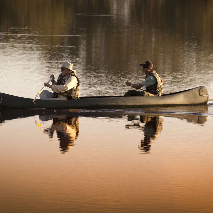 Zwei Männer in einem Kanu auf einem ruhigen Gewässer des Refúgio Ecológico Caiman im Pantanal, Brasilien, während sie die friedliche Landschaft und das spiegelnde Wasser genießen.