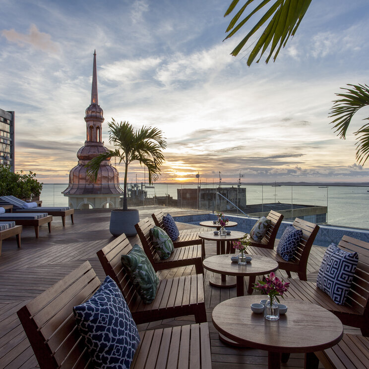 Fera Palace Hotel Dachterrasse mit Holzliegen und Blick auf die Allerheiligenbucht bei Sonnenuntergang in Salvador.
