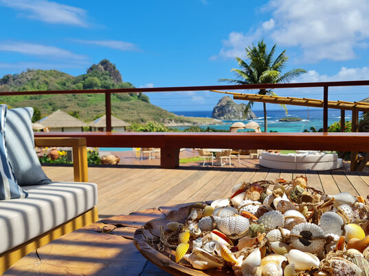 Balkon der Pousada Solar dos Ventos auf Fernando de Noronha mit Muscheldekoration und Blick auf das Meer und Hügel.