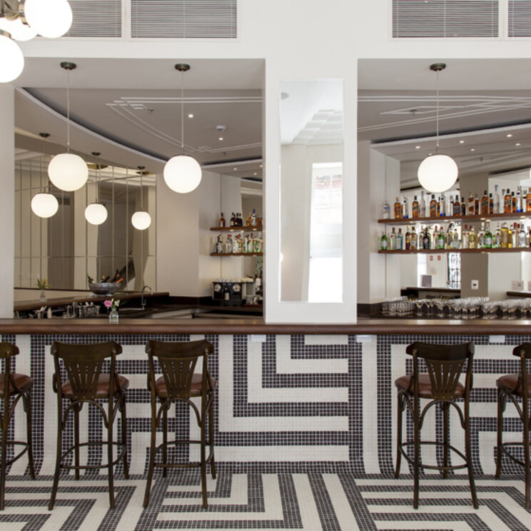 Hotelbar mit gemustertem Fliesenspiegel am Tresen, dunklen Barhockern und hängenden Kugelleuchten in Salvador.