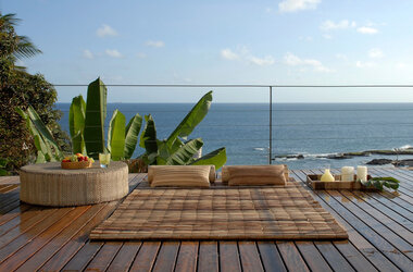 Holzterrasse mit Bambusmatte, Sitzkissen und Bananenpflanzen vor dem blauen Atlantik in Salvador