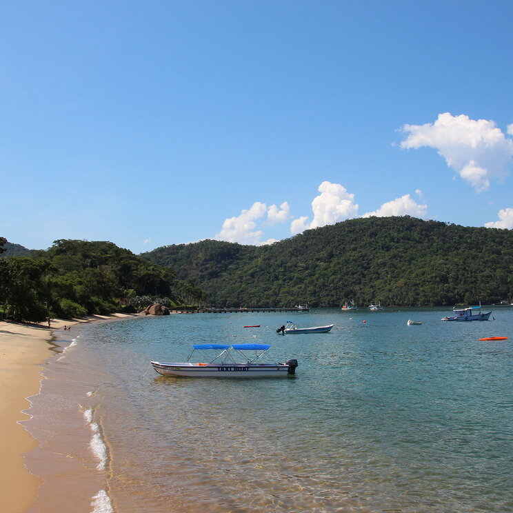 Blick auf die Küste von Ilha Grande, Brasilien, mit majestätischen Bergen im Hintergrund und bunten Booten am Strand.