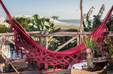Vila Kalango Jericoacoara: Rote Hängematte auf Holzbalkon mit Blick auf Dünen, Palmen und Meer in Brasilien.