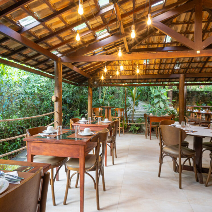 Überdachter Restaurantbereich mit Holztischen und Stühlen unter einem Gebälkdach in der Pousada Naturalia.