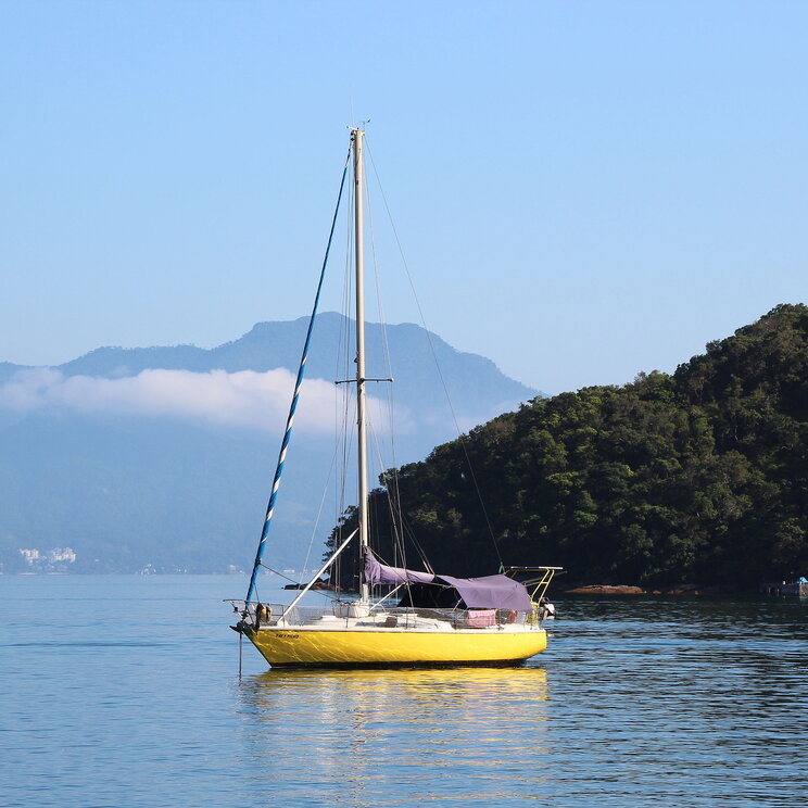 Gelbes Segelboot, das ruhig im Wasser vor der Küste von Ilha Grande, Brasilien, schaukelt, umgeben von der beeindruckenden Berglandschaft und der unberührten Natur der Region.
