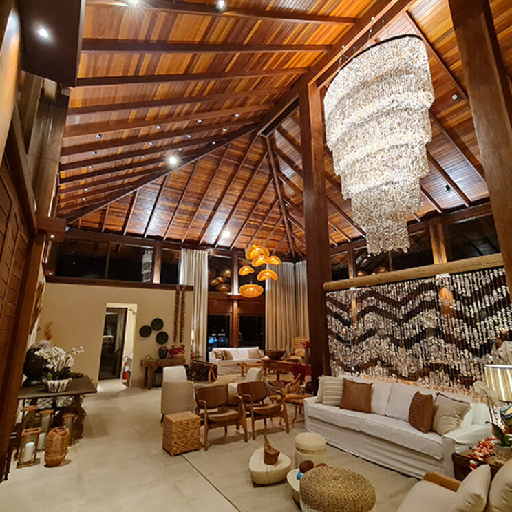 Großzügige Hotel-Lobby mit hohen Holzdecken, Muschel-Raumteiler und elegantem Kronleuchter bei Nacht.