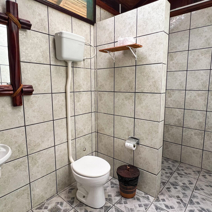 Hell gefliestes Badezimmer in einem Bungalow von Amazon Village mit Waschbecken, WC und Spiegel mit Holzrahmen.