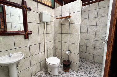 Hell gefliestes Badezimmer in einem Bungalow von Amazon Village mit Waschbecken, WC und Spiegel mit Holzrahmen.
