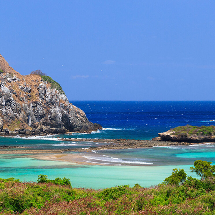 Tropische Bucht mit türkisfarbenem Wasser und markanter Felsinsel vor Fernando de Noronha.