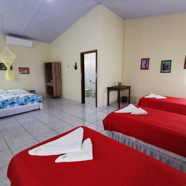 Zimmer im Hotel UeSo Pantanal, Brasilien: Ein komfortables Familienzimmer mit roten Betten und modernen Annehmlichkeiten, ideal für einen Aufenthalt im Pantanal.