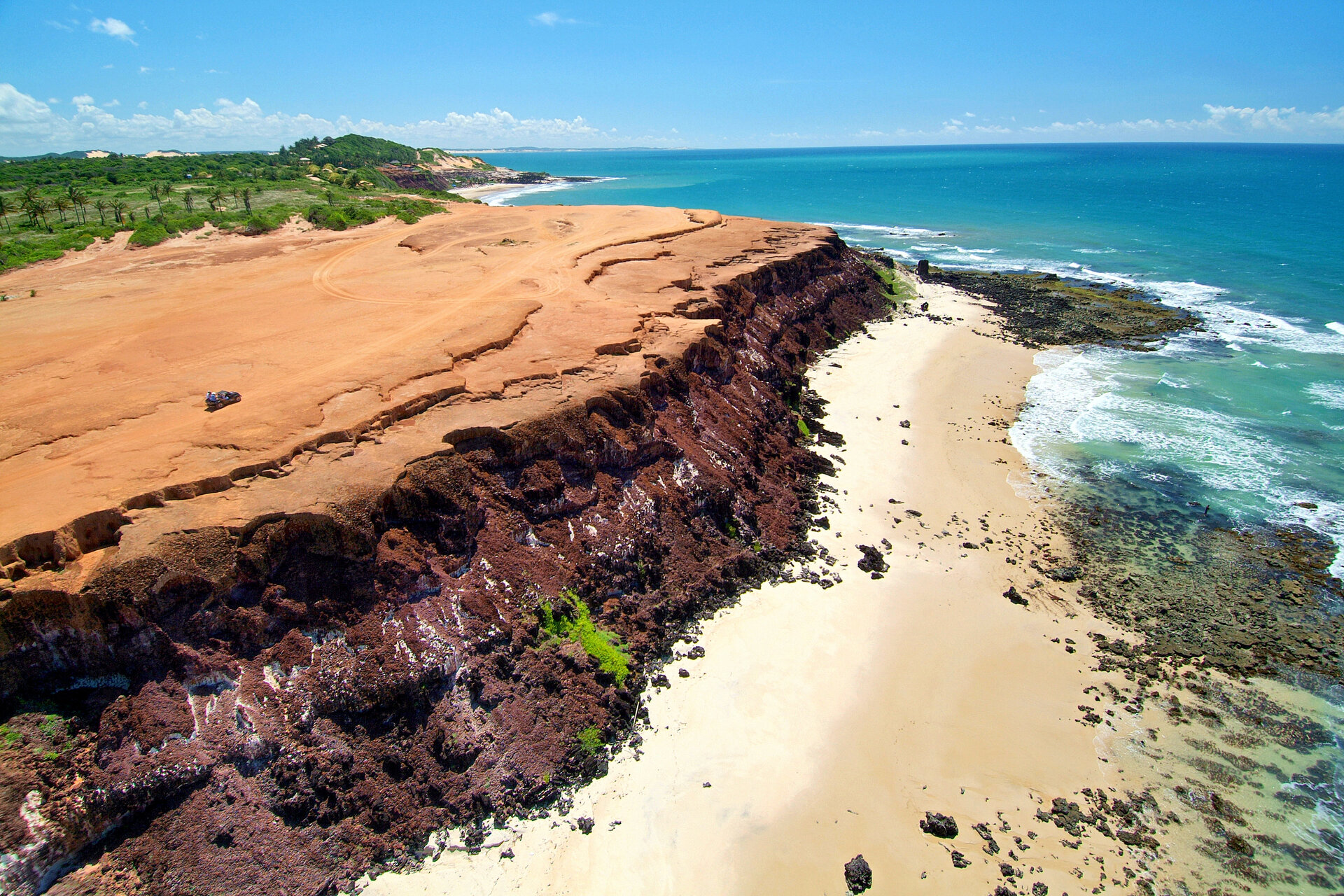 Luftaufnahme der rötlichen Steilküste Chapadão de Pipa über einem hellen Sandstrand in Tibau do Sul, Rio Grande do Norte.