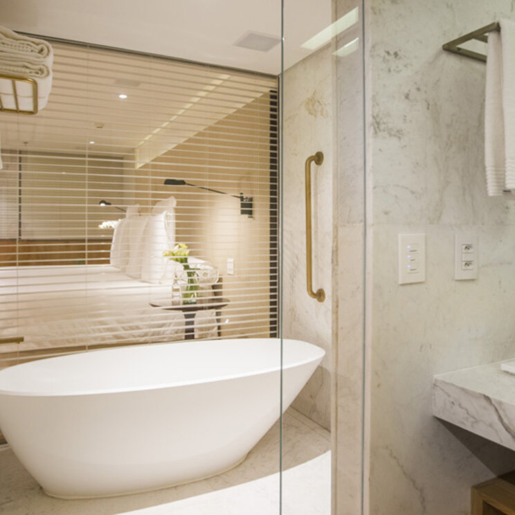 Modernes Marmorbad im Emiliano Rio mit freistehender Badewanne und Blick durch ein Fenster in den Schlafbereich.