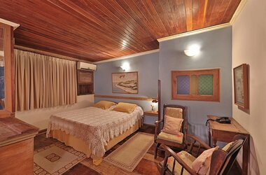 Schlafzimmer mit Doppelbett, blauen Wänden, Holzdecke und zwei Sesseln in der Pousada do Amparo.