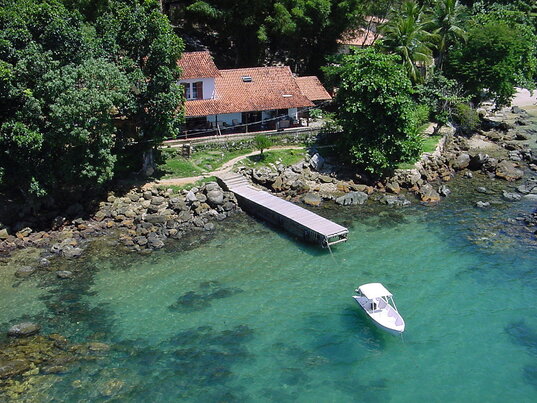 Bootssteg und kleines Boot im klaren Wasser vor dem Sagu Mini Resort am bewaldeten Ufer, Ilha Grande, Brasilien.