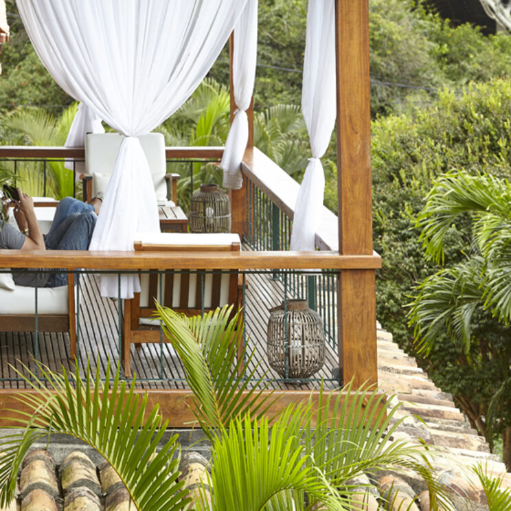 Überdachter Balkon im PortoBay Buzios mit weißen Vorhängen, Holzmöbeln und Blick auf tropische Palmen in Brasilien.