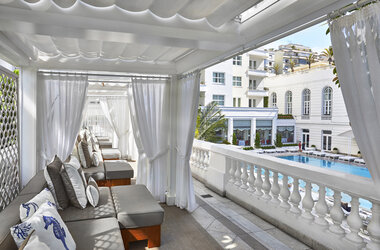 Exklusive Gazebos mit weissen Vorhaengen und Polstermoebeln auf einer Terrasse mit Blick auf den Hotelpool.