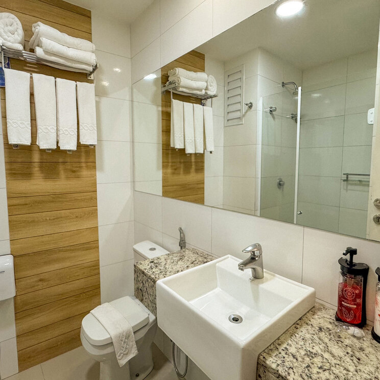 Modernes Badezimmer mit weißem Waschbecken, Wandspiegel und Holzverkleidung im Vivaz Cataratas, Foz do Iguaçu.
