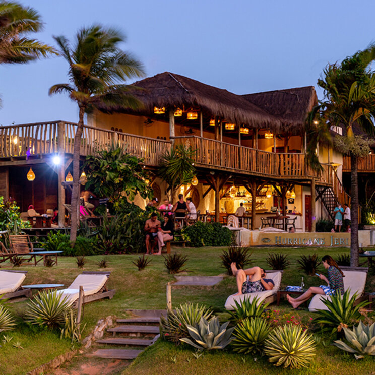 Beleuchtetes Hotelgebaeude bei Daemmerung mit Garten, Liegestuehlen und Palmen im Hurricane Jeri, Brasilien.