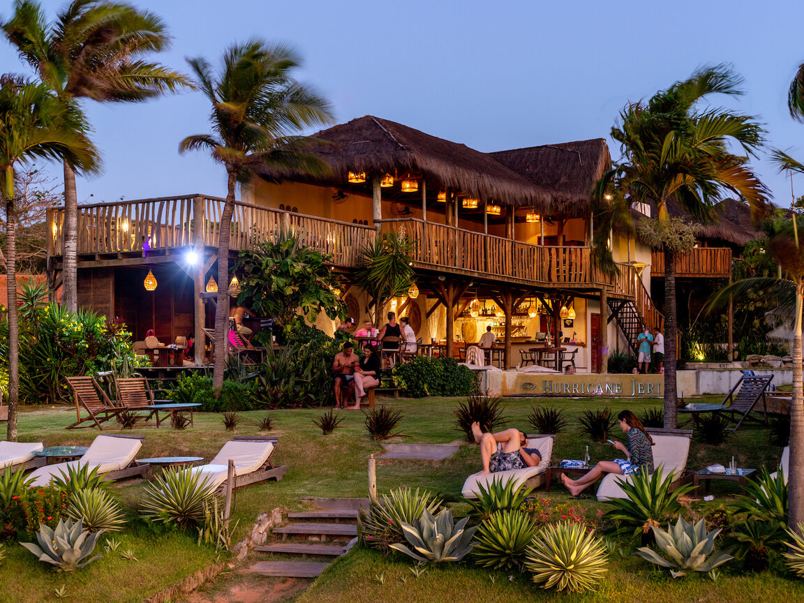 Beleuchtetes Hotelgebaeude bei Daemmerung mit Garten, Liegestuehlen und Palmen im Hurricane Jeri, Brasilien.