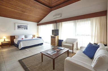 Schlaf- und Wohnbereich der Royal Suite im PortoBay Buzios mit Holzdecke, Doppelbett, Sofa und hellem Fliesenboden.
