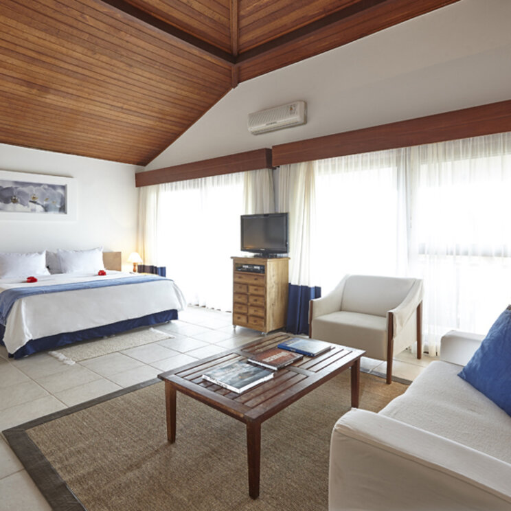 Schlaf- und Wohnbereich der Royal Suite im PortoBay Buzios mit Holzdecke, Doppelbett, Sofa und hellem Fliesenboden.