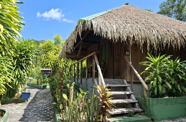 Rustikaler Holzbungalow mit Strohdach und Aussentreppe in der Gartenanlage von Amazon Village.