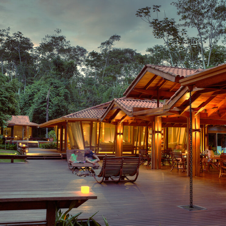 Beleuchtete Holzterrasse und Bungalows am Abend vor Regenwaldkulisse in der Cristalino Lodge, Brasilien.