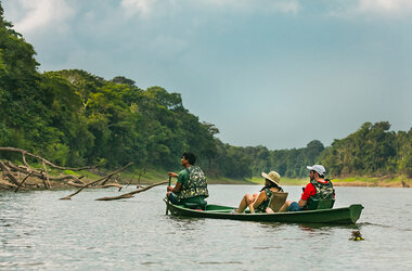 Drei Personen in einem gruenen Kanu auf einem Fluss im Amazonas-Regenwald bei der Uakari Lodge, Brasilien.