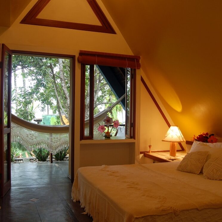Gemütliches Zimmer der Pousada Pitinga in Porto Seguro, Brasilien, mit Blick auf eine Hängematte auf der Veranda und tropischer Umgebung.