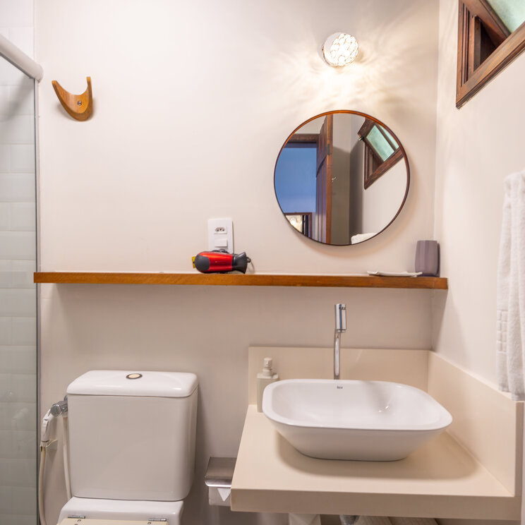 Modernes Badezimmer mit weißem Aufsatzwaschbecken, rundem Spiegel und Glasdusche in der Pousada Naturalia.