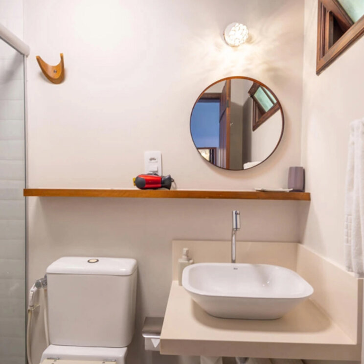 Modernes Badezimmer mit weißem Aufsatzwaschbecken, rundem Spiegel und Glasdusche in der Pousada Naturalia.