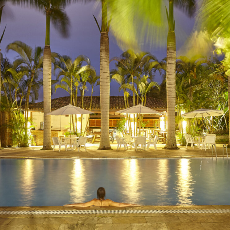 Beleuchteter Außenpool im PortoBay Buzios bei Nacht mit Palmen, Sonnenschirmen und Blick auf die Poolbar in Brasilien.
