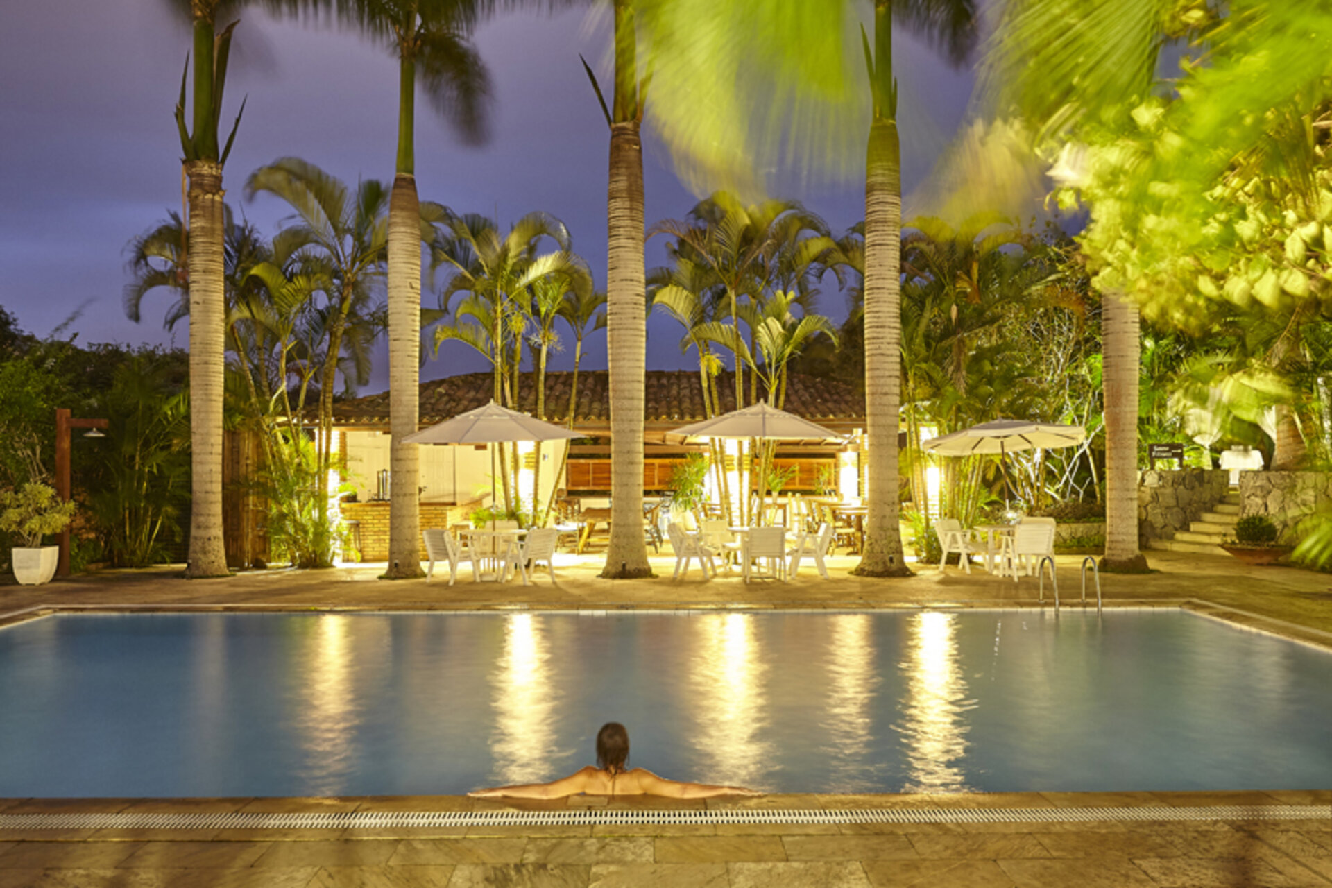 Beleuchteter Außenpool im PortoBay Buzios bei Nacht mit Palmen, Sonnenschirmen und Blick auf die Poolbar in Brasilien.
