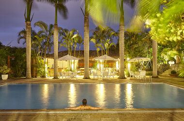 Beleuchteter Außenpool im PortoBay Buzios bei Nacht mit Palmen, Sonnenschirmen und Blick auf die Poolbar in Brasilien