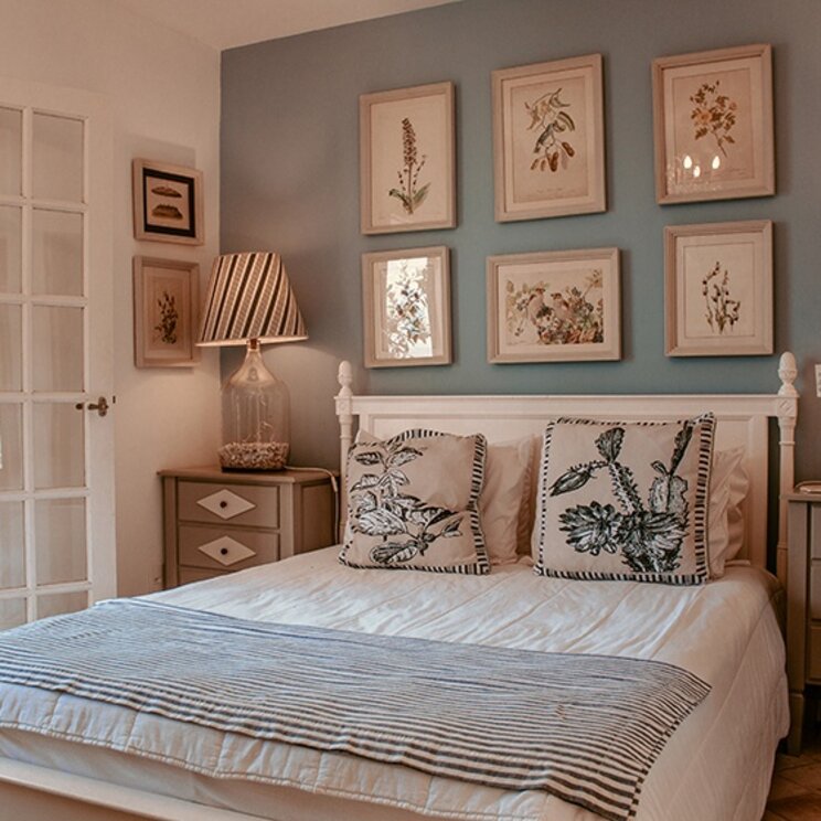 Hellblaues Schlafzimmer mit weißem Bett, botanischen Bildern und gläsernen Nachttischlampen in Buzios.