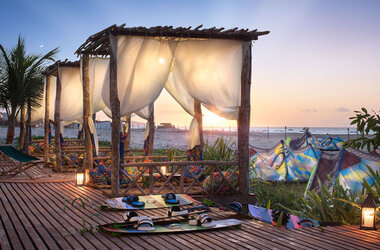 Gazebos mit weißen Vorhängen auf einem Holzdeck am Strand bei Sonnenuntergang in Prea.