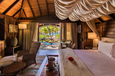 Bungalow-Schlafzimmer mit Holzdach und Blick auf Palmen und Meer im Nannai Resort, Porto de Galinhas.