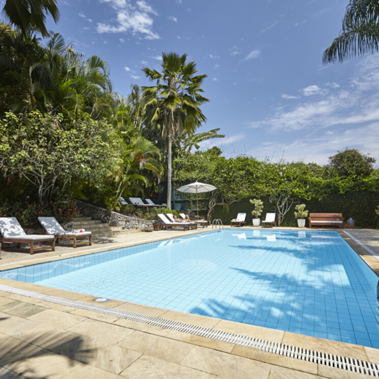 Großer Außenpool im PortoBay Buzios, Brasilien, umgeben von Sonnenliegen, Palmen und tropischer Vegetation.