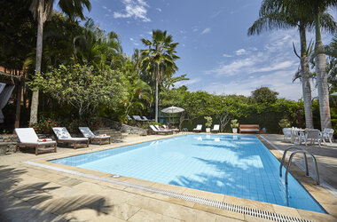 Großer Außenpool im PortoBay Buzios, Brasilien, umgeben von Sonnenliegen, Palmen und tropischer Vegetation.