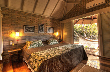 Gemütliches Schlafzimmer im Refúgio Ecológico Caiman im Pantanal, Brasilien, mit einem einladenden Bett, warmen Farbtönen und direktem Zugang zur Terrasse mit Hängematte.