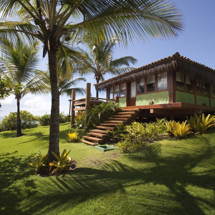 Holzbungalow auf Pfählen mit Treppe, umgeben von Rasen und Palmen im Txai Resort, Itacaré, Brasilien.