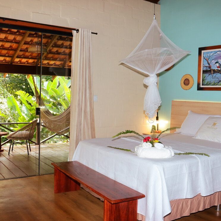 Schlafzimmer im Bungalow mit Doppelbett und Blick durch Glasschiebetüren auf die Veranda.