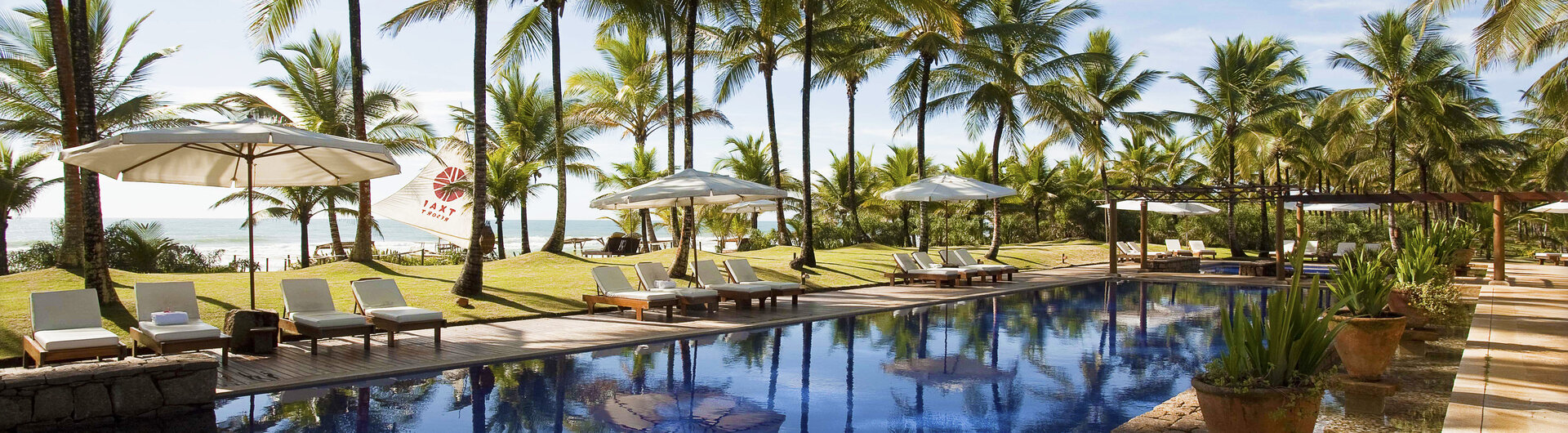 Großer blauer Außenpool im Hotel Txai Resort Itacaré, umgeben von tropischen Pflanzen und hohen Palmen.