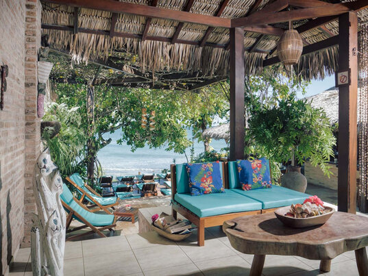 Offener Aufenthaltsraum mit türkisfarbenem Daybed, rustikalem Holztisch und Blick auf den Strand von Jericoacoara.