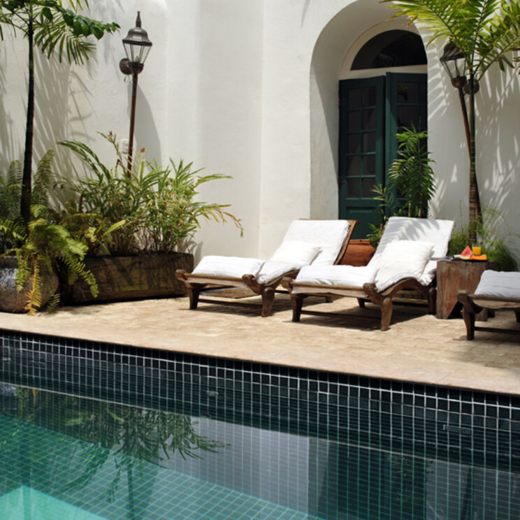 Türkisfarbener Pool mit Sonnenliegen, Palmen und weißer Fassade im Innenhof der Villa Bahia in Salvador.